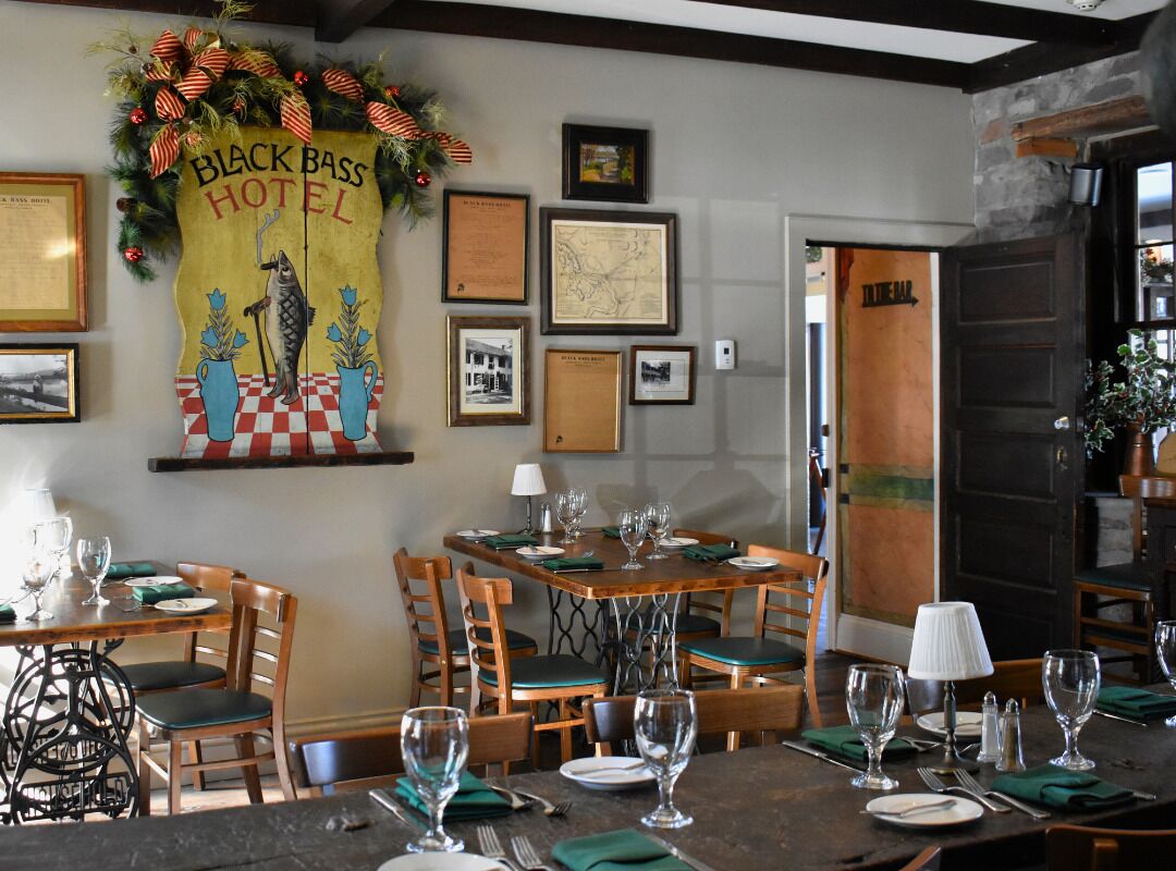 Un espace repas avec des tables et des chaises en bois, des tableaux encadrés accrochés au mur et une enseigne indiquant « Hôtel Black Bass ».
