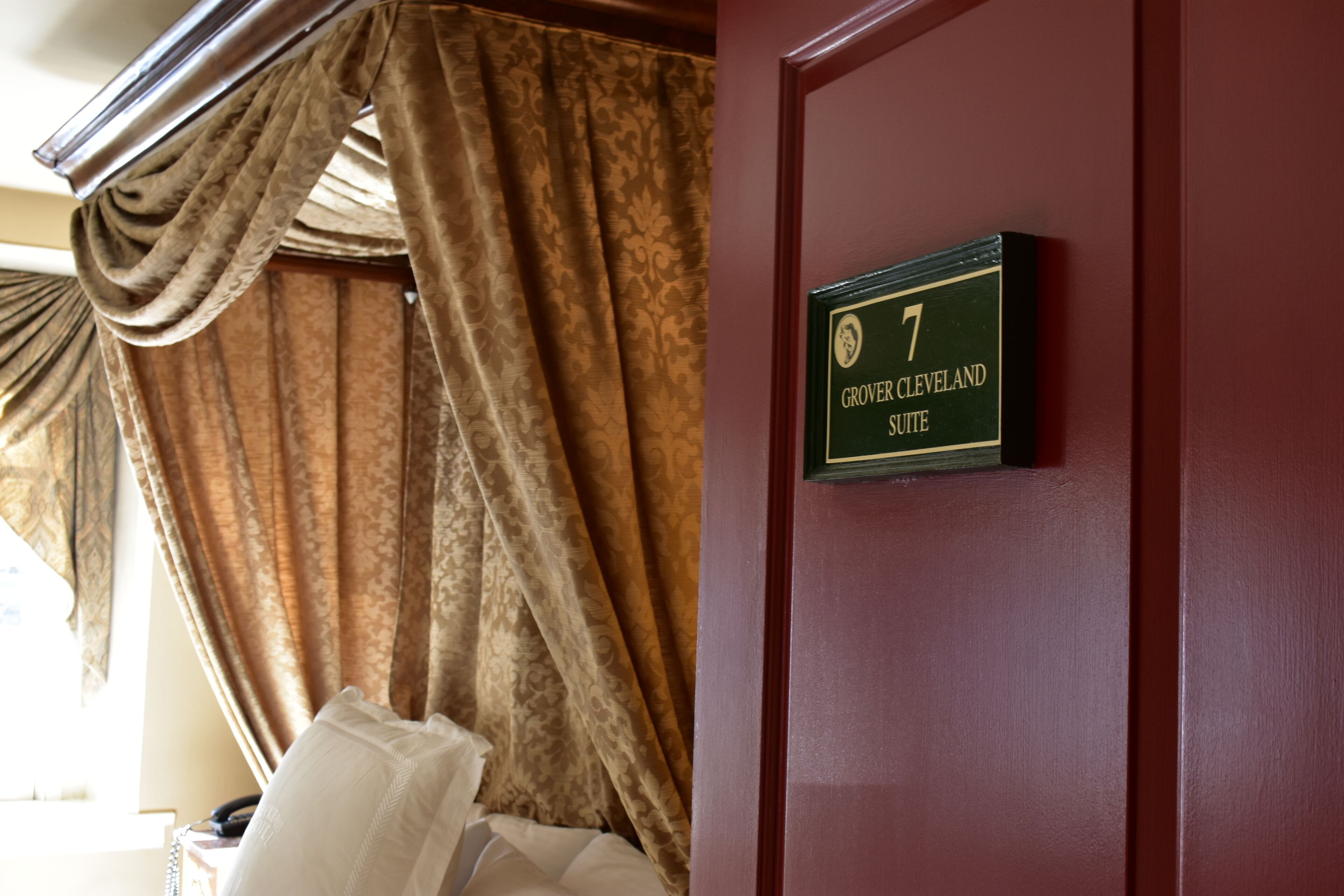 Una habitación con cama, ventana con cortinas y puerta con un cartel que indica el número 7.