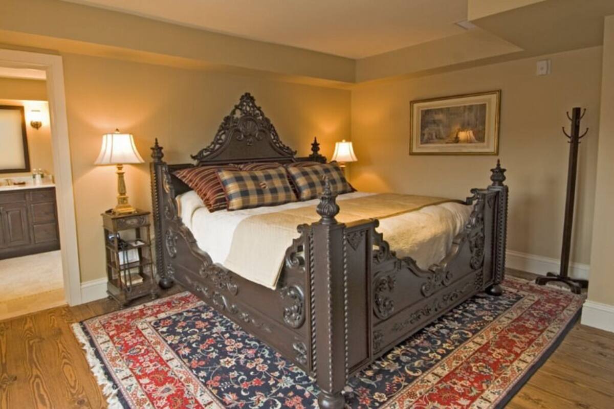 A bedroom with a large bed, two bedside lamps, a framed picture on the wall, and a floor lamp.