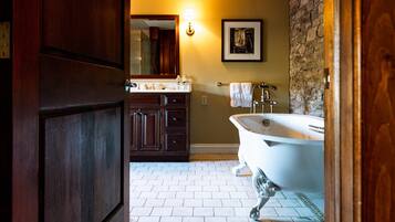Une salle de bain avec une baignoire sur pieds, des meubles en bois, un mur d’accent en pierre et un sol carrelé.