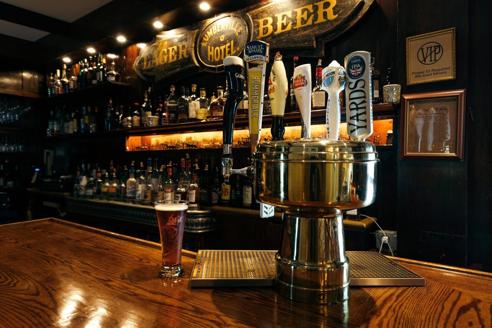 Eine Barbereich mit Zapfanlage für verschiedene Biersorten, ein Bierglas und im Hintergrund eine Auswahl an Flaschen.
