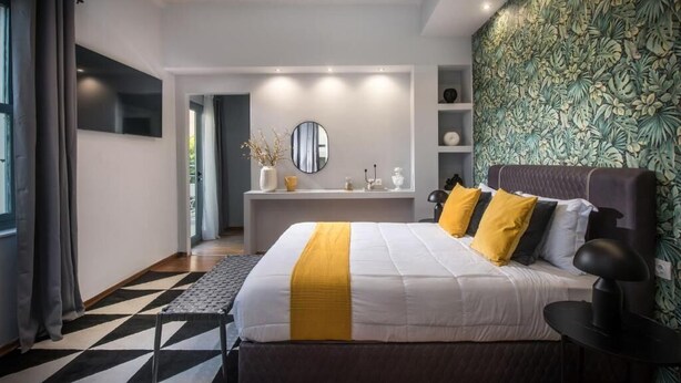 Un dormitorio moderno con una cama grande, una mesita de noche, un espejo y una pared con un estampado de hojas.