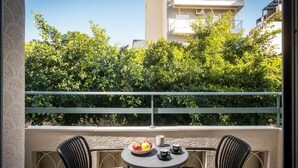 Un balcón con dos sillas de mimbre negro, una mesita redonda con un frutero, una jarra blanca y dos tazas.