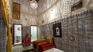 A room with patterned walls, a bed with a red bedspread, a small table, and a hanging light fixture. - Riad Lala Kenza (Fes)