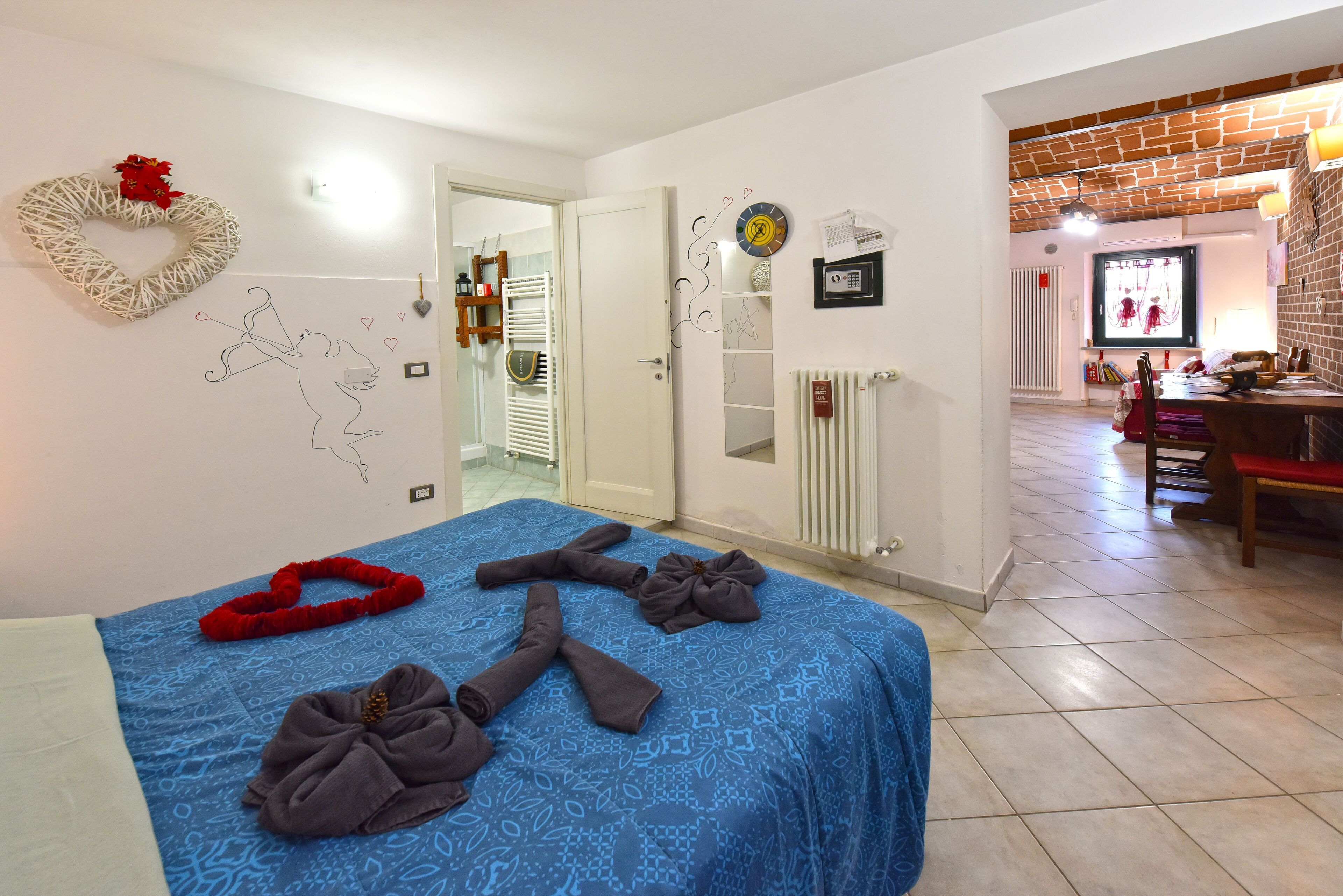 Une chambre d’hôtel avec une couvre-lit à motifs bleus, une décoration murale en forme de cœur, une horloge et un mur en briques.