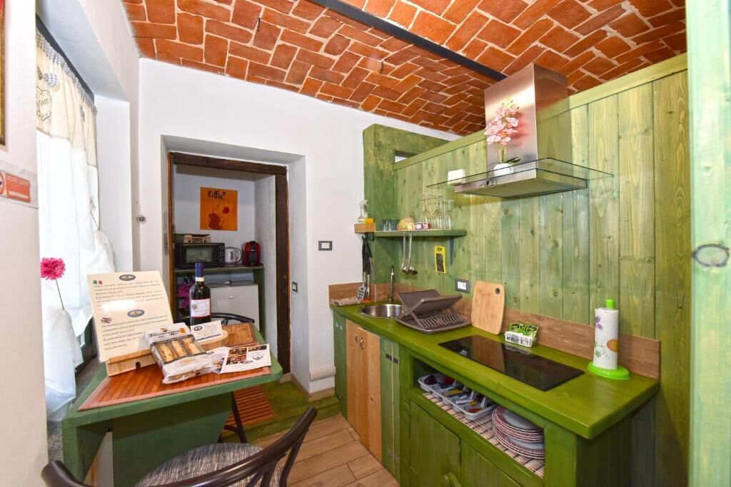 A compact kitchen with green cabinetry, a brick ceiling, and a small dining area with a table and chairs.