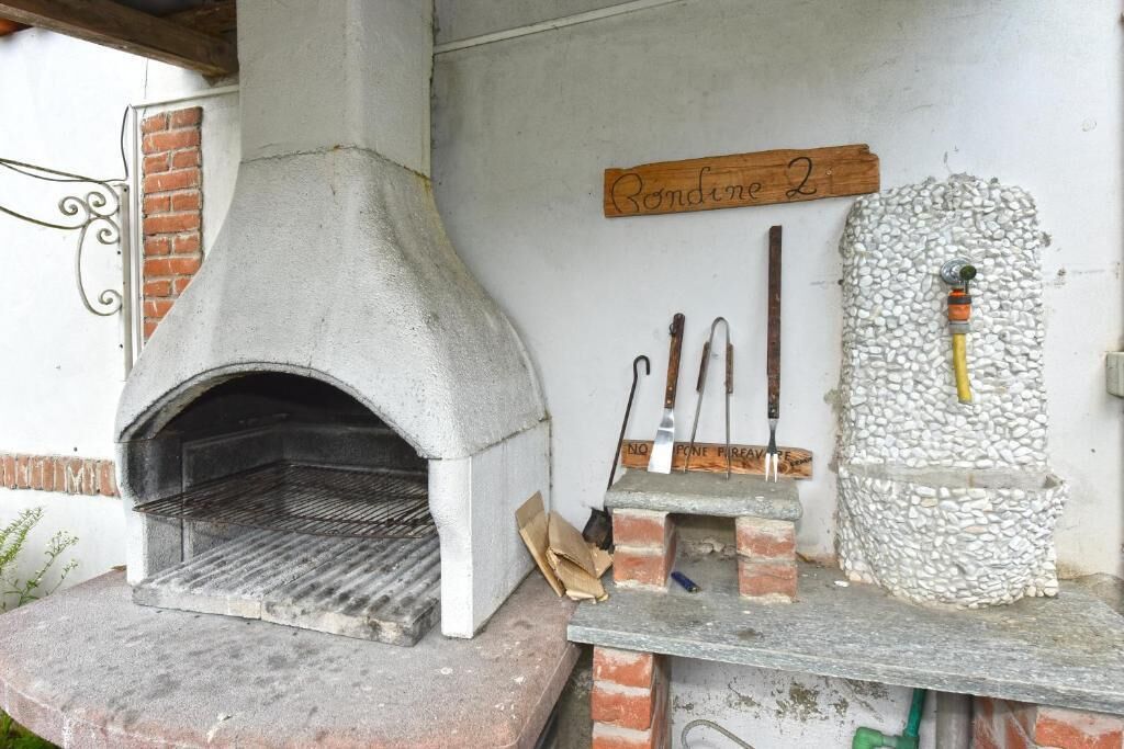 Un four extérieur en pierre, avec une base en briques, une enseigne en bois au-dessus et un mur de pierre doté d’une cheminée.