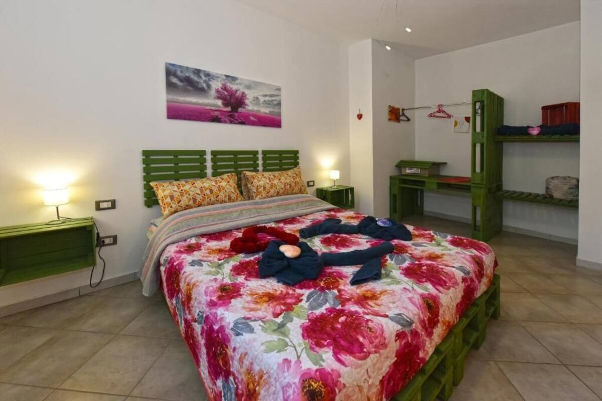 A bedroom with a floral bedspread, green headboard, bedside tables with lamps, and a bunk bed with storage.