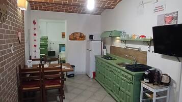 A kitchen with a brick ceiling, green cabinets, a dining table with chairs, and a television mounted on the wall.