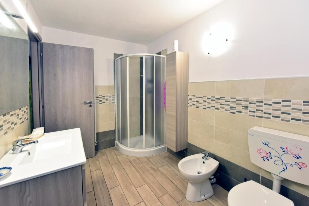 A bathroom with a shower enclosure, a sink, a bidet, and a toilet.
