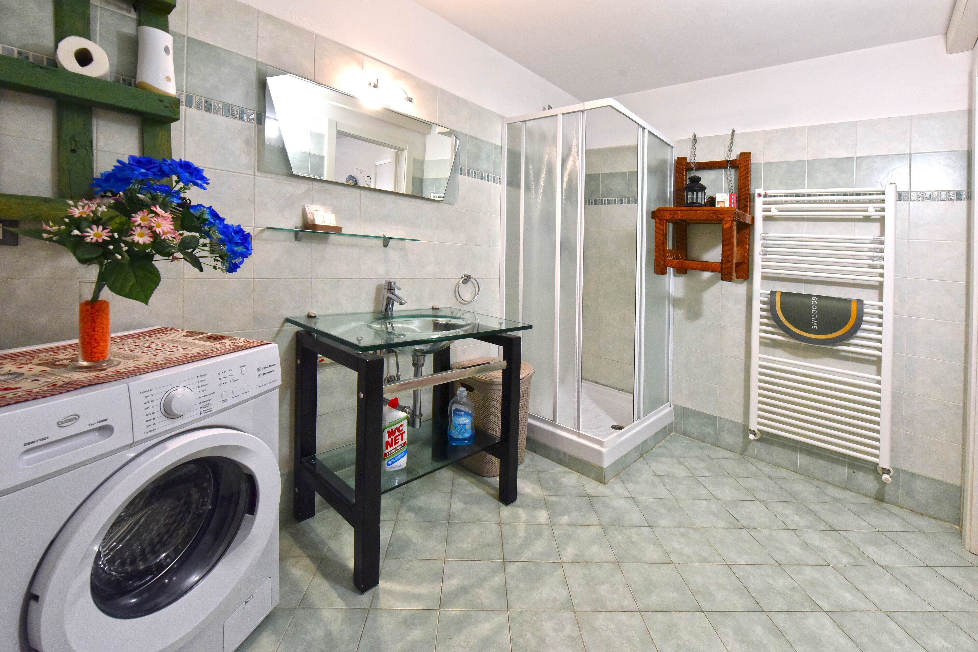 A modern bathroom with a glass sink, a washing machine, a shower enclosure, and a towel rack.