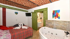 Une chambre d’hôtel avec un lit, une grande baignoire, une porte verte et un tableau abstrait aux couleurs vives.
