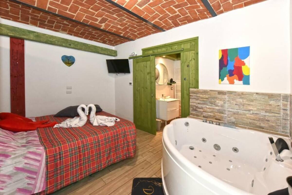 A hotel room with a bed, a large bathtub, a green door, and a colorful abstract painting.