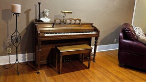 A grand piano in a room with wooden flooring, a dark-colored sofa, and a wall-mounted lamp. - Spacious 4-bedroom house in perfect Marshall for your getaway (Marshall)