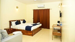 Una habitación de hotel con cama, escritorio, silla, aire acondicionado y ventilador de techo.