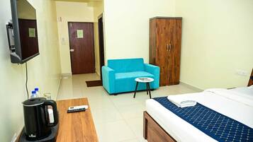 Habitación de hotel con cama, sofá azul, mueble de madera, una mesita con un control remoto y una tetera sobre una mesa de madera.