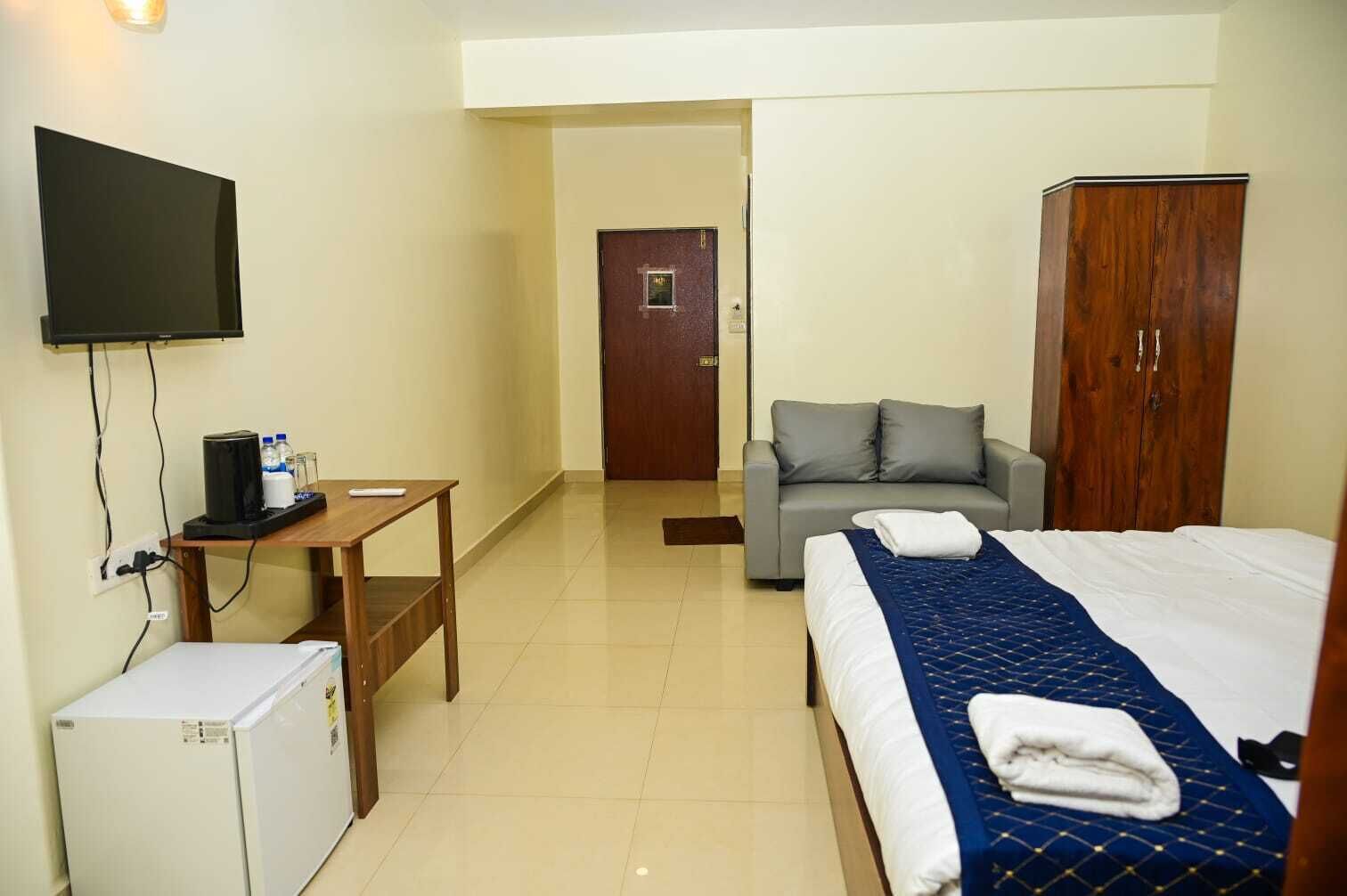 A hotel room with a bed, a desk with a computer, a television, a wardrobe, and a sofa.