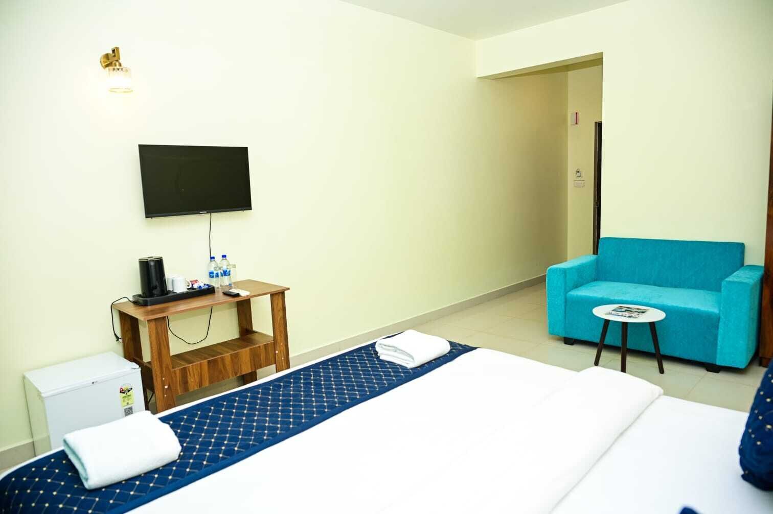 A hotel room with a bed, a TV, a coffee maker, a water dispenser, a blue sofa, and a small table.