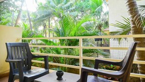 Un balcón con dos sillas de plástico negro y una mesita pequeña, con vista a un jardín exuberante con altas palmeras.