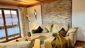 A living room with a stone wall, a sofa, a coffee table, and a window with curtains. - Vacation home Benedikt Füssen, Eschach FW2 (Füssen)