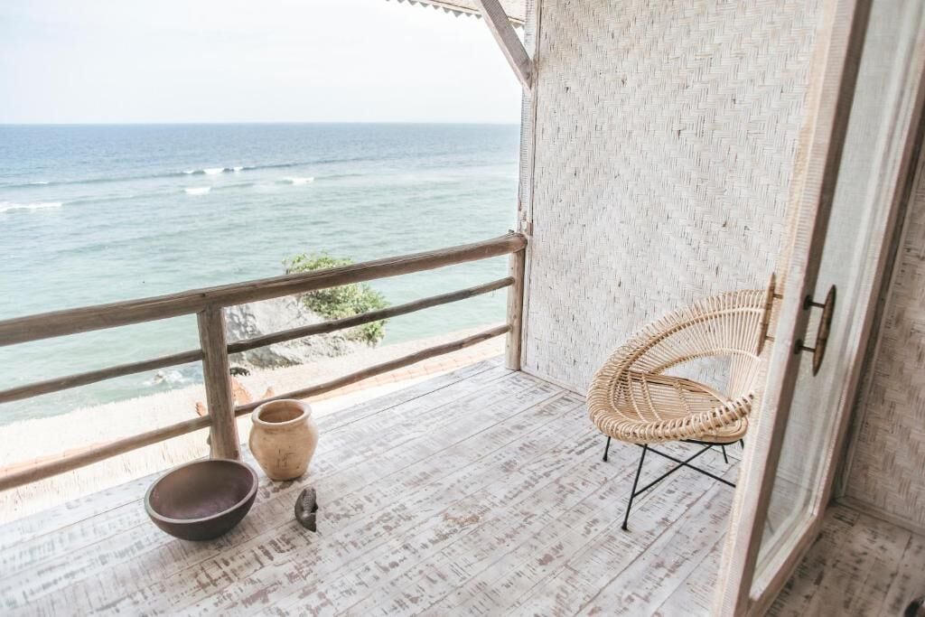Un balcon avec un fauteuil en osier, deux bols et une vue sur l’océan.