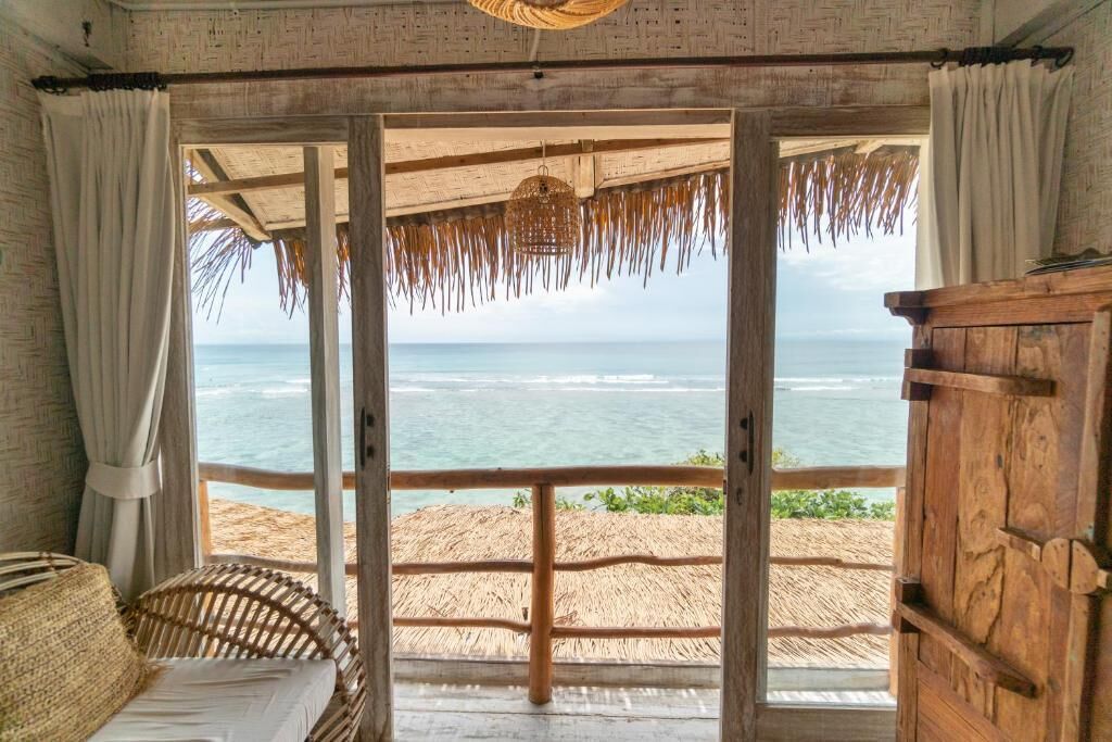 A room with a view of the ocean, a straw roof, and a wooden door.