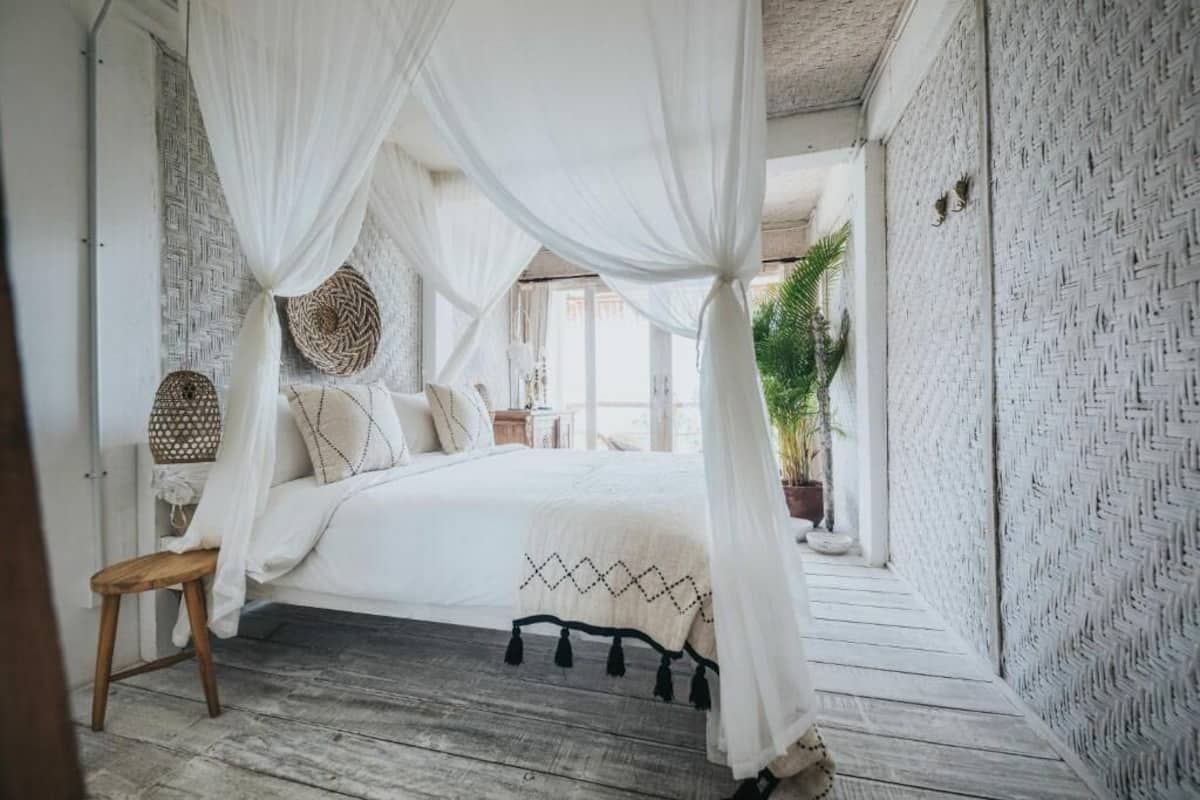 A bedroom with a canopy bed, woven wall decor, and a wooden floor.