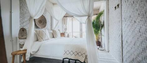 A bedroom with a canopy bed, woven wall decor, and a wooden floor.
