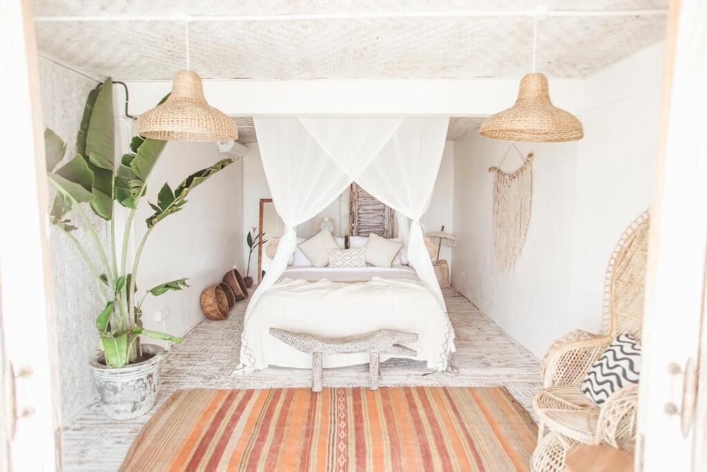 Une chambre à coucher avec un lit à baldaquin, une chaise en rotin et une plante en pot.