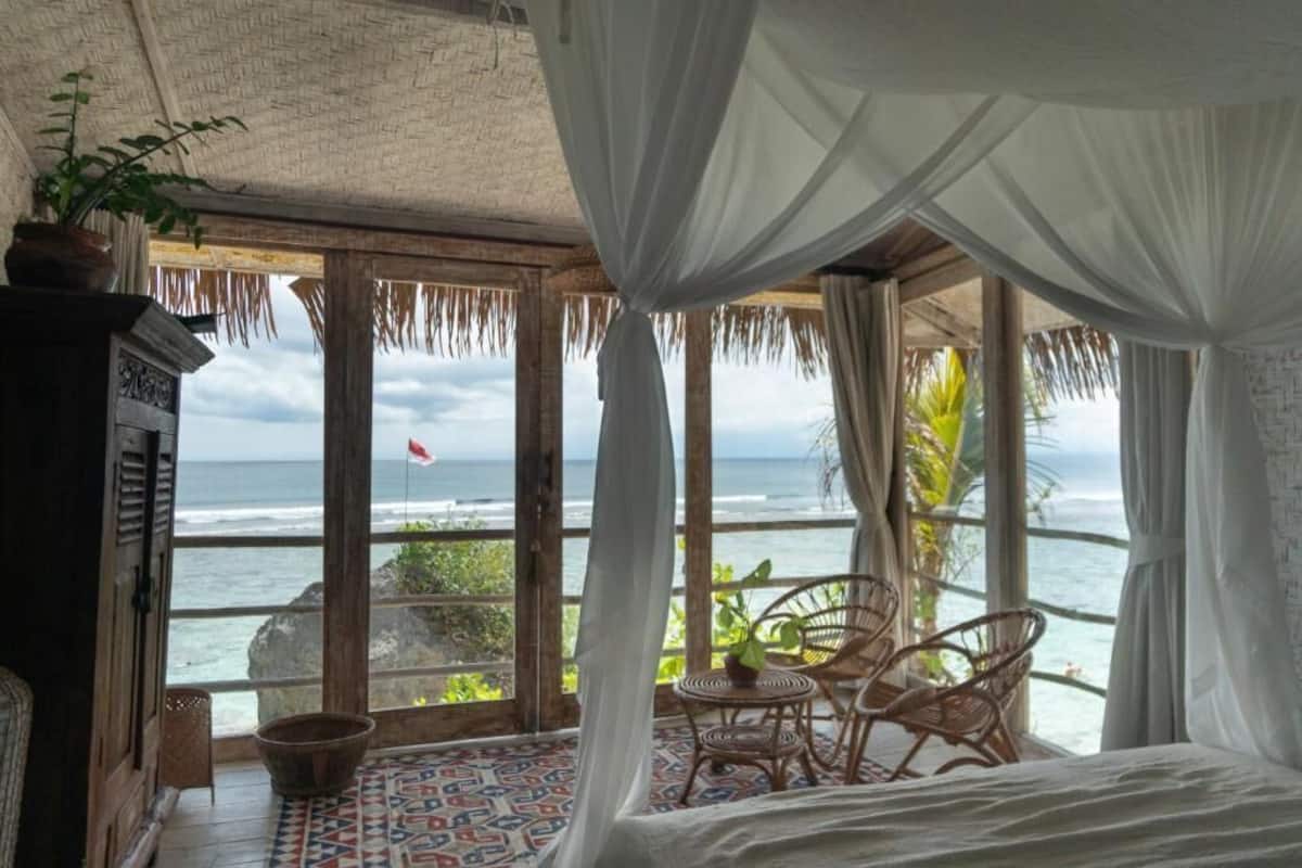 A room with a bed, a table, and chairs, overlooking the ocean.