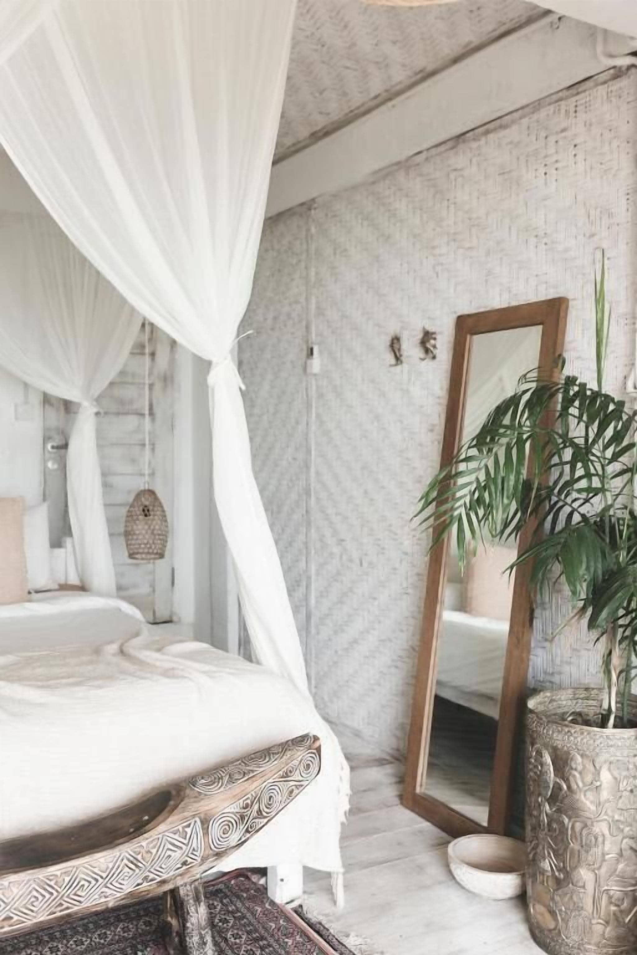 A bedroom with a bed under a white canopy, a large mirror, a potted plant, and a textured wall.