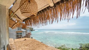 A coastal hotel with thatched roofs, a view of the ocean, and a building with a balcony overlooking the sea. - Dreamsea Uluwatu (Pecatu)