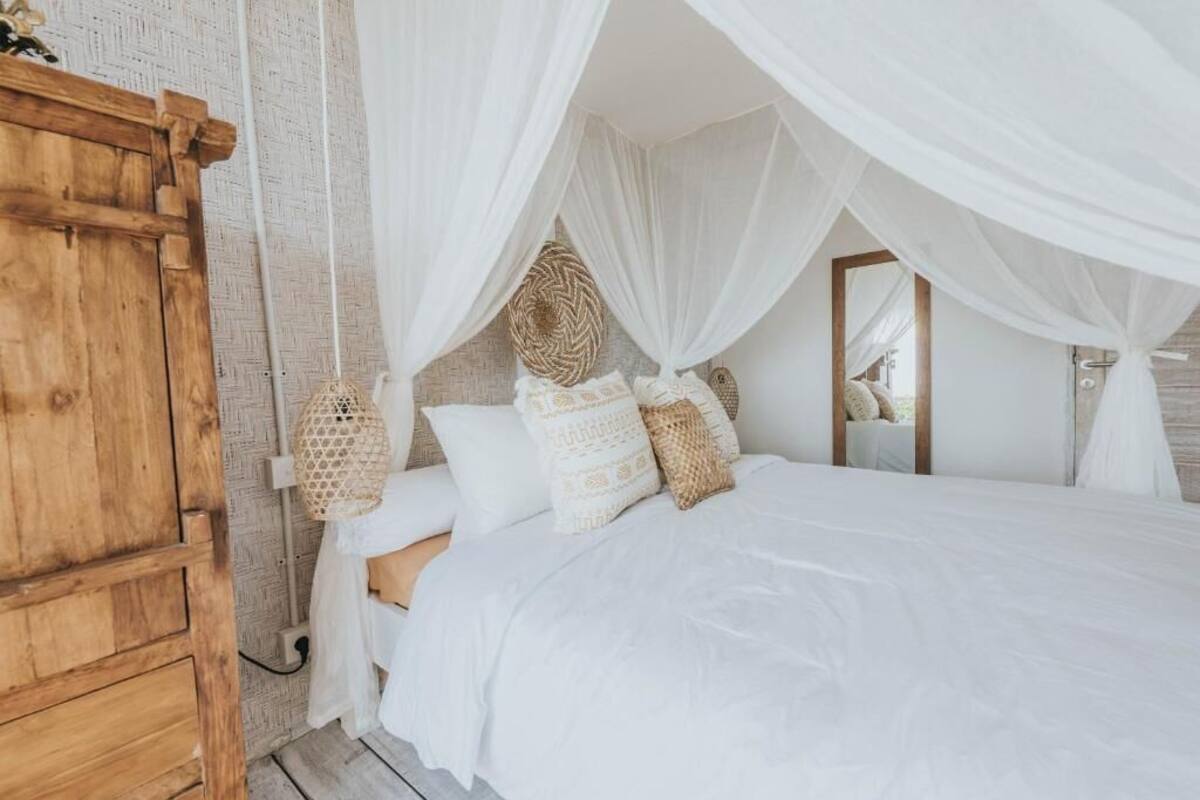 A bedroom with a bed under a canopy, a wooden wardrobe, and a woven basket.