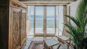 A room with a large wooden cabinet, a woven chair, and a view of the ocean through a glass door. - Dreamsea Uluwatu (Pecatu)