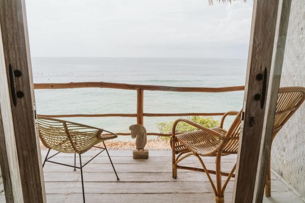 A wooden deck with two wicker chairs facing a view of the ocean.