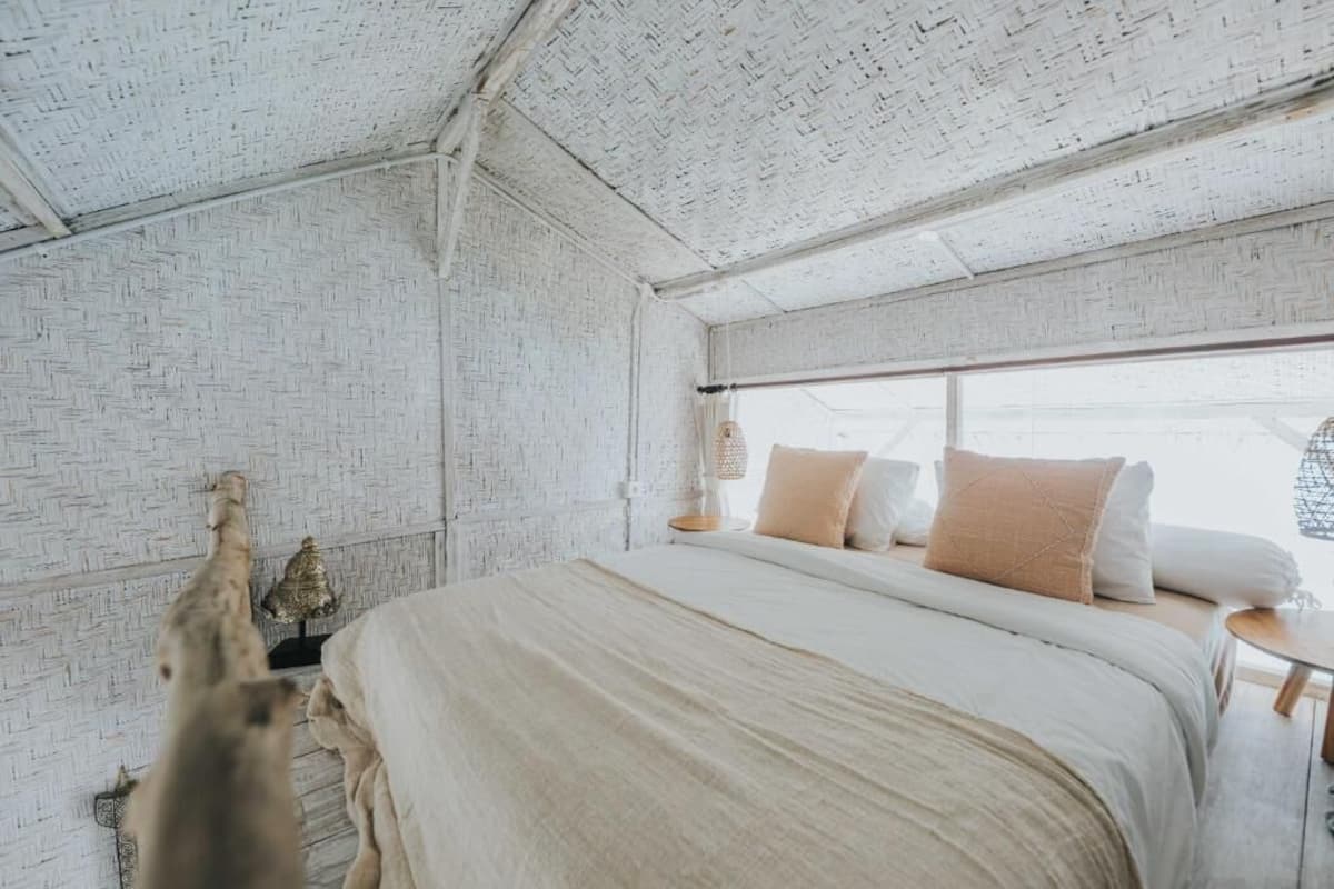 A bedroom with a brick-patterned ceiling, a large bed with multiple pillows, a small table, and a hanging light fixture.