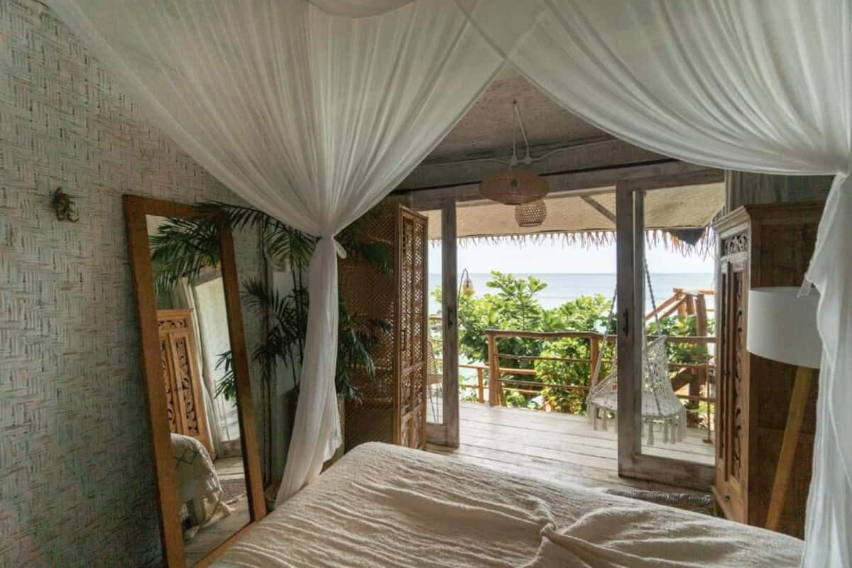 A bedroom with a bed, a large mirror, and a balcony with a view of the sea.
