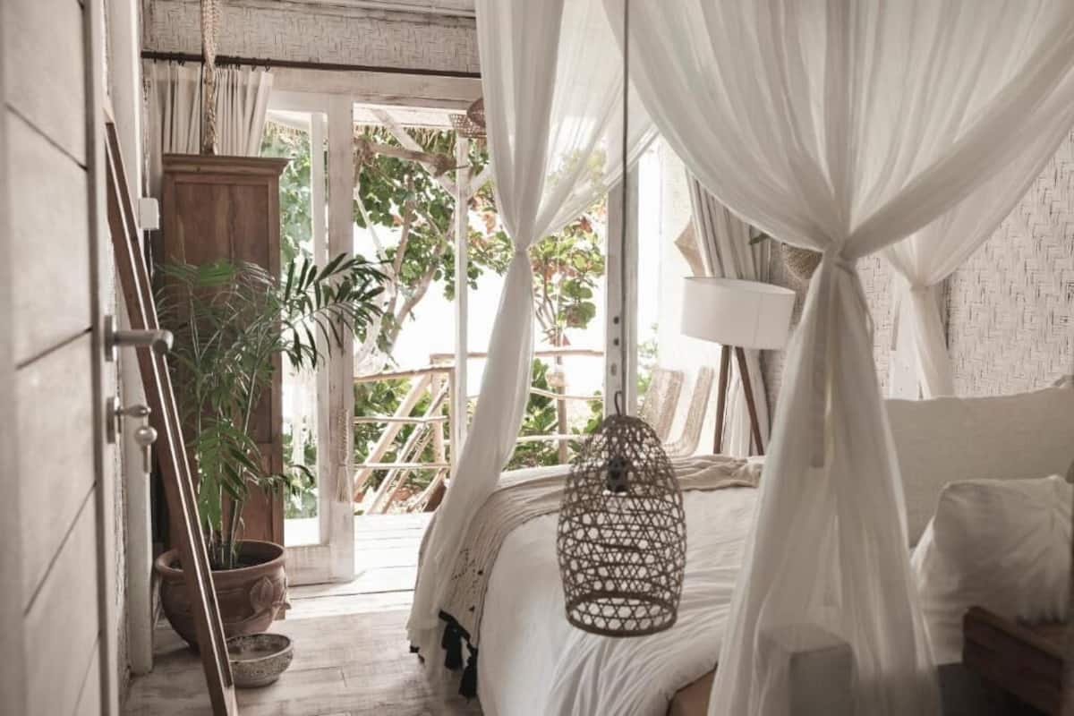 A bedroom with a bed, a hanging light fixture, a potted plant, and a view of the outdoors.
