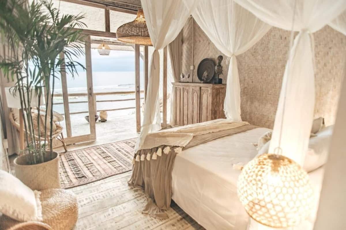 A bedroom with a large bed, a canopy, a view of the beach, and a rustic wooden cabinet.