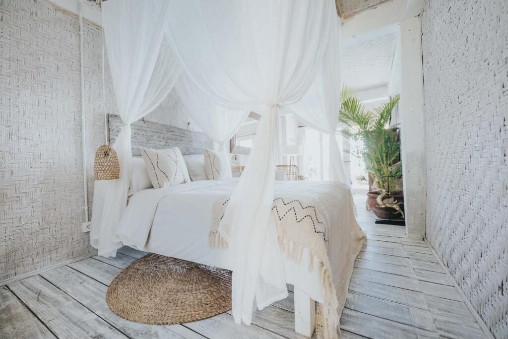 Une chambre à coucher avec un lit sous un dais, un tapis tissé et une plante en pot.