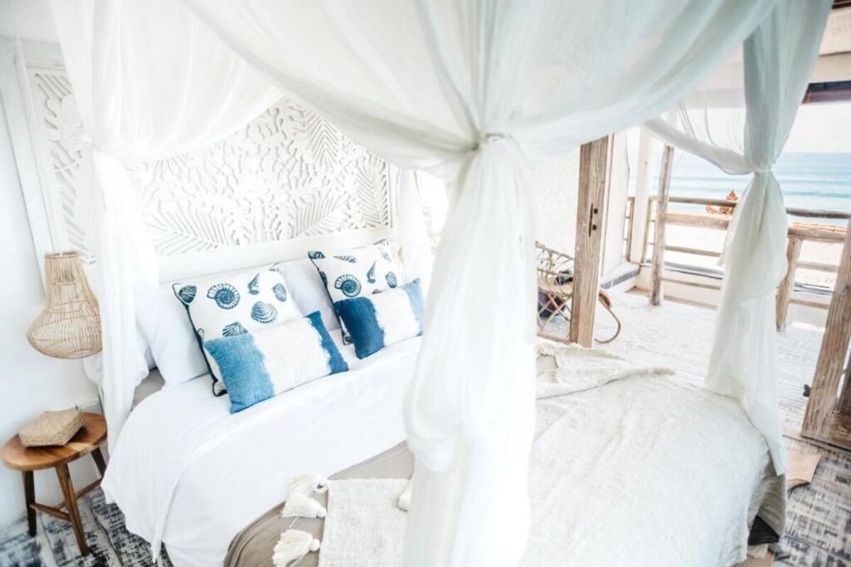 A bed with a canopy, white bedding, and patterned pillows.