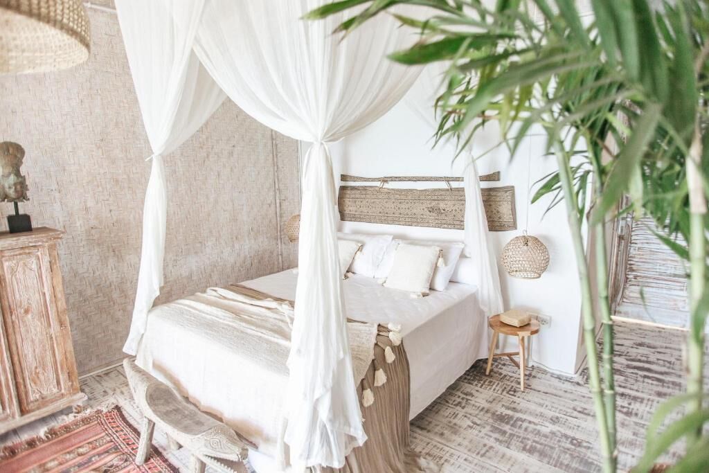 A bed with a canopy, a small stool, a woven wall hanging, and a rustic wooden cabinet.