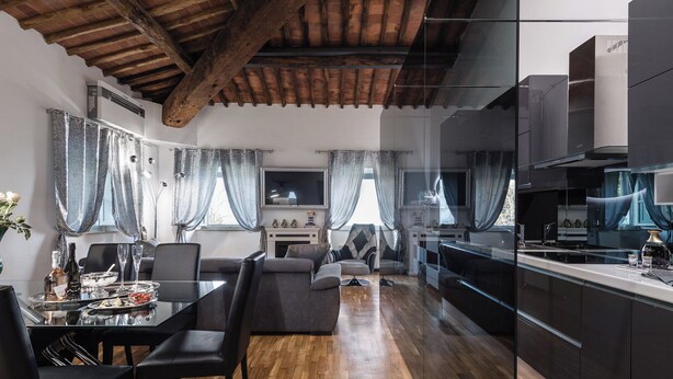 A modern kitchen with dark cabinetry, a central island, and a dining area with a table and chairs. - Giotto (Matraia)