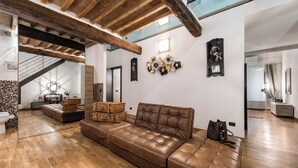 A spacious living area with a leather sofa, wooden flooring, and a staircase with exposed beams. - Giotto (Matraia)