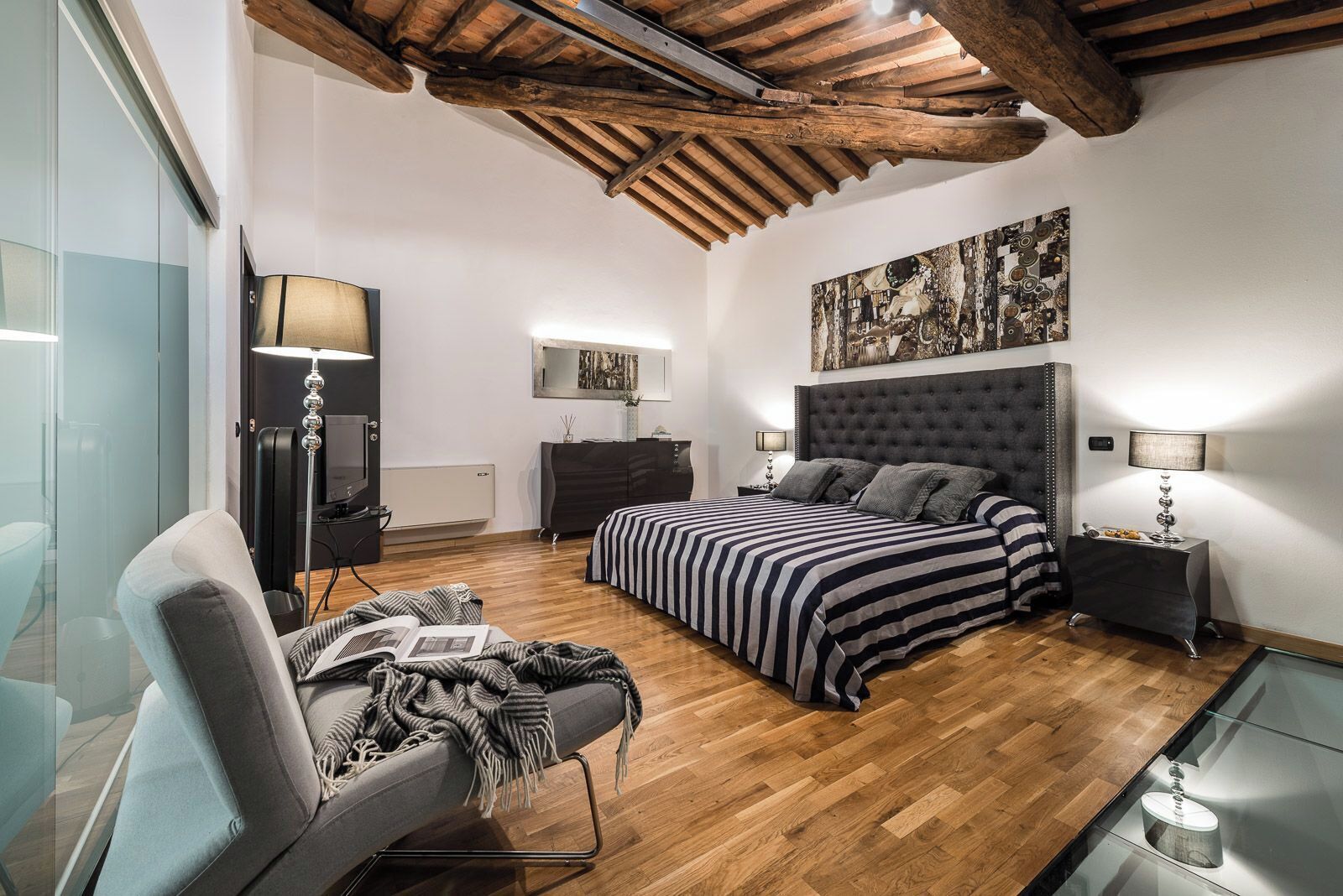 A modern bedroom with a large bed, a TV, a desk, and a chair.