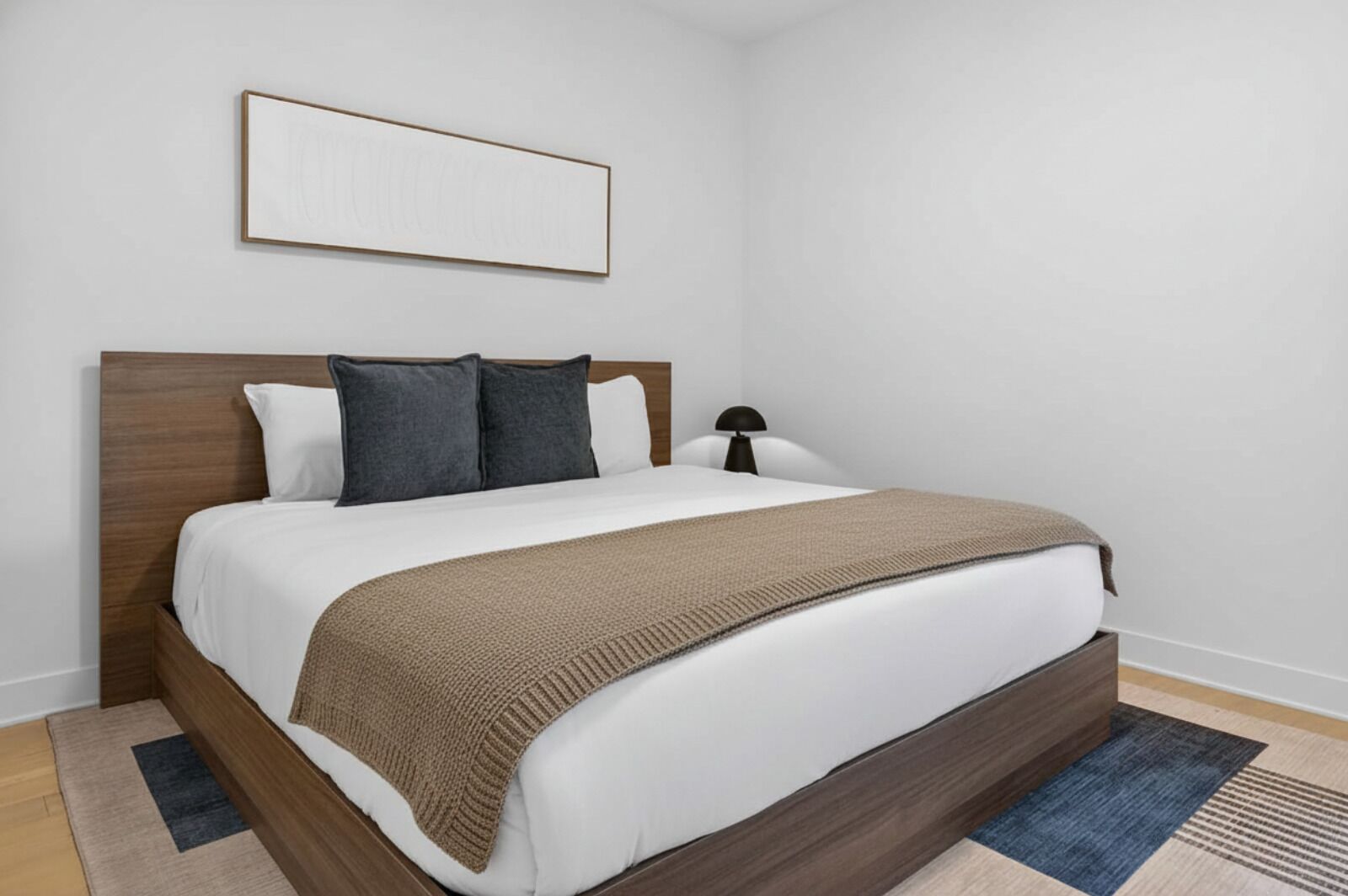 Una cama bien hecha con una manta marrón, sábanas blancas y dos almohadones oscuros.