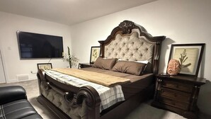 A bedroom with a large bed, a TV mounted on the wall, a dresser, and a chair. - A home away from home. YEG retreat (Edmonton)