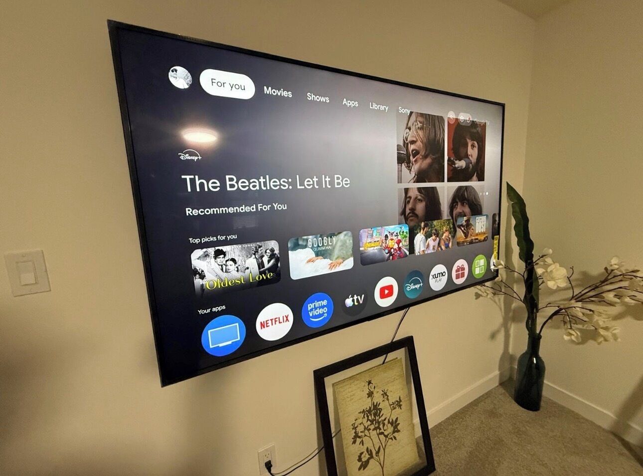 Televisor de pantalla plana montado en una pared, mostrando una interfaz de servicio de transmisión con diversas opciones de contenido e iconos de aplicaciones.