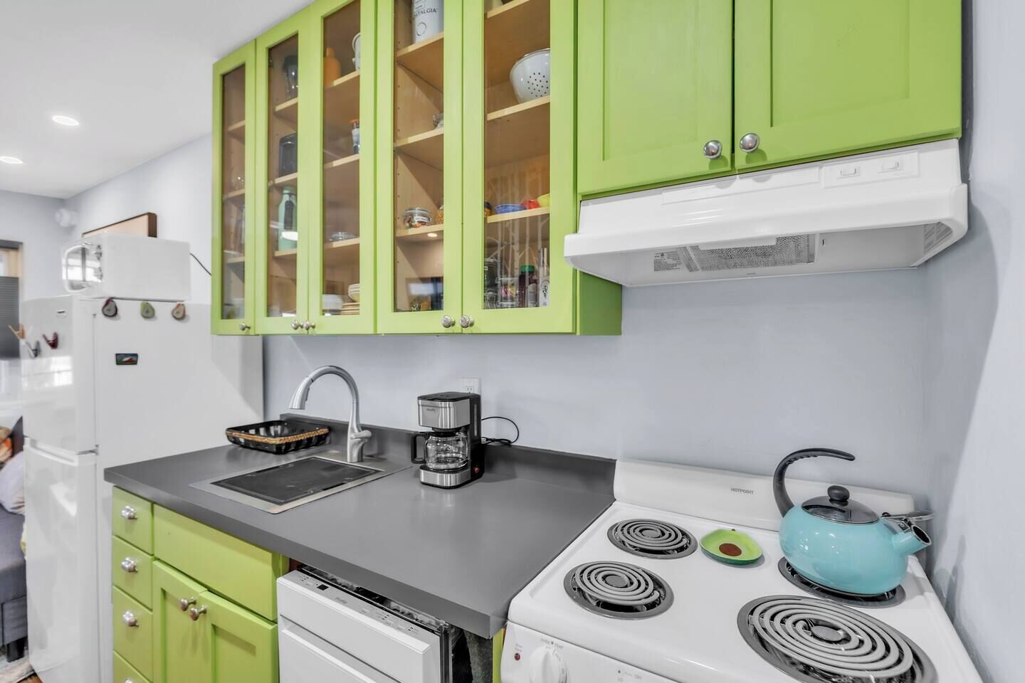 A kitchen with green cabinets, a white stove, and a kettle.