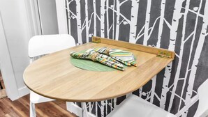 Uma pequena mesa de madeira com uma cadeira branca, um tecido colorido e uma parede com padrão de árvore em preto e branco.